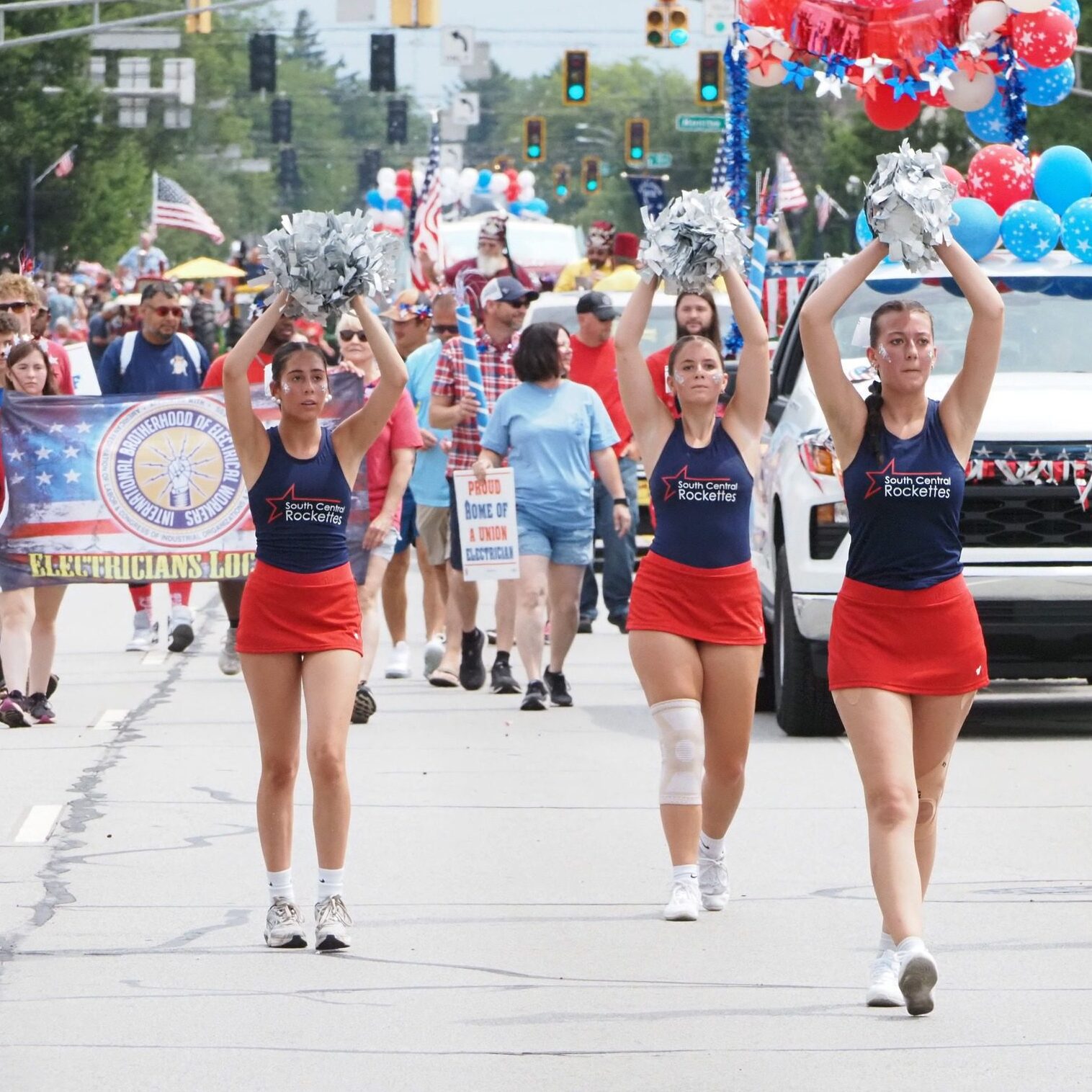 South Central Rockettes cheerleaders performing with silver pom-poms at the Kiwanis Fourth of July Parade in LaPorte, Indiana, with parade spectators and union banners behind them.